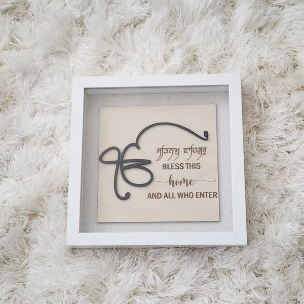 A glass enclosed shadow box measuring 9x9 inch is home to wood engraved sign with a 3D style.  The wordings say :  Ek Onkar. Satnam Waheguru.  Bless this home and all who enter.