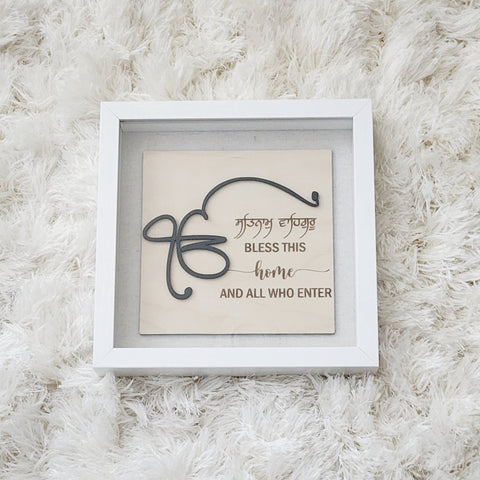 A glass enclosed shadow box measuring 9x9 inch is home to wood engraved sign with a 3D style.  The wordings say :  Ek Onkar. Satnam Waheguru.  Bless this home and all who enter.